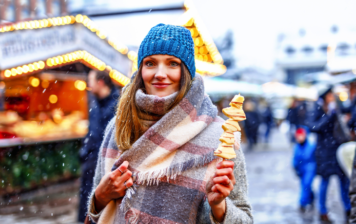 Frau isst auf einem traditionellen deutschen Weihnachtsmarkt mit weißer Schokolade überzogene Früchte am Spieß