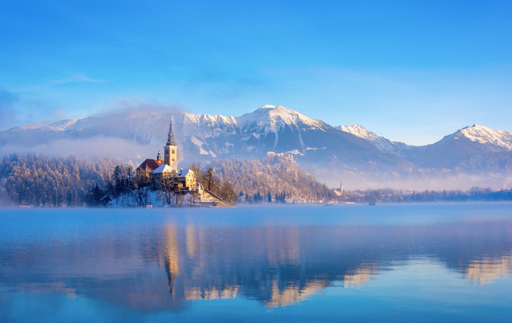 Bleder See an einem sonnigen Wintermorgen mit klarem Himmel und schneebedeckten Bergen
