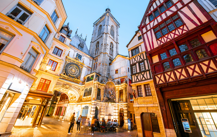 Straßenansicht mit beleuchteten Gebäuden und dem berühmten Uhrturm in der Dämmerung in der Altstadt von Rouen in Frankreich